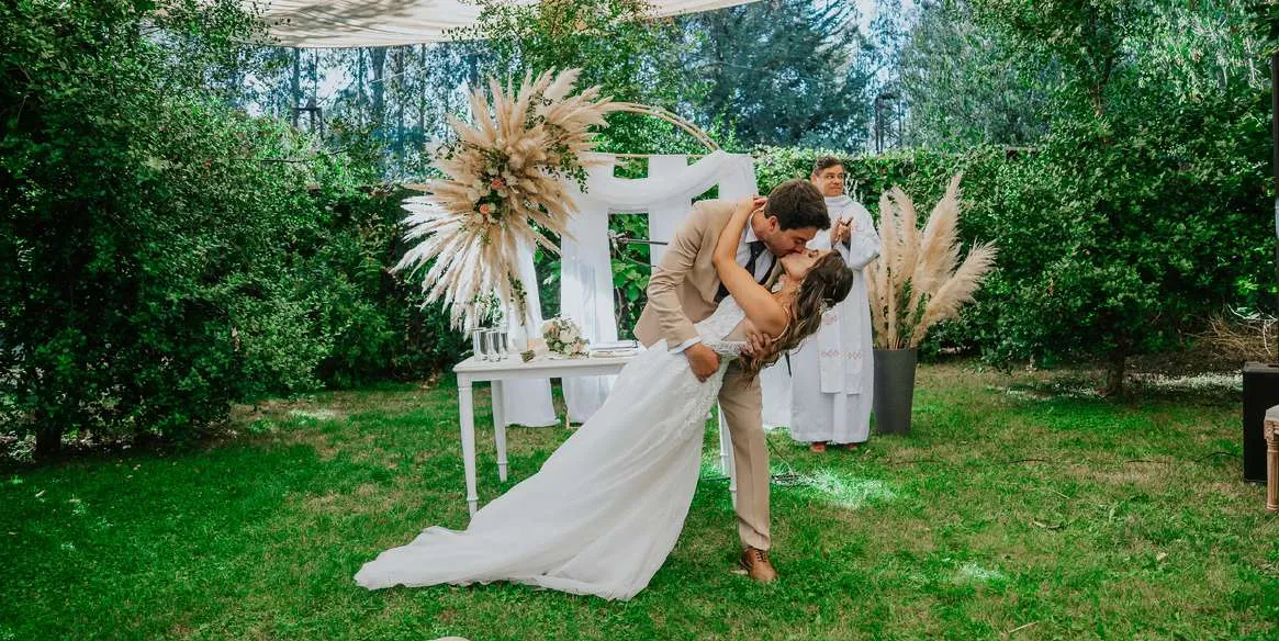 Novios besándose frente al arco de ceremonia en el parque